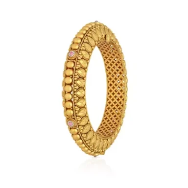 A gold bangle with intricate designs and embedded pink stones.