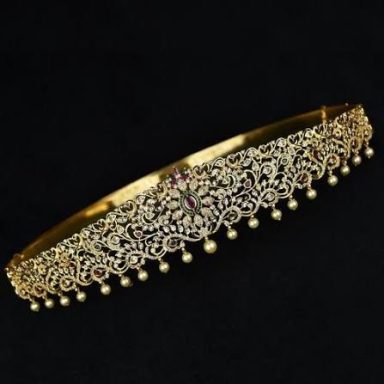 Gold decorative tiara with intricate floral designs and hanging pearls.