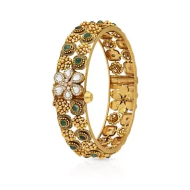 Gold bangle adorned with floral patterns and green stones, featuring a central flower design.