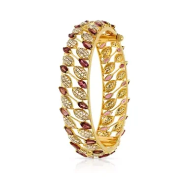 Gold bangle adorned with red and white gemstones, featuring an intricate leaf design.